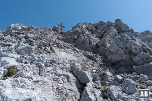 Oberhalb der Verschneidung linksdrehend im leichten Fels (I) und über viel Schutt zum Gipfelkreuz